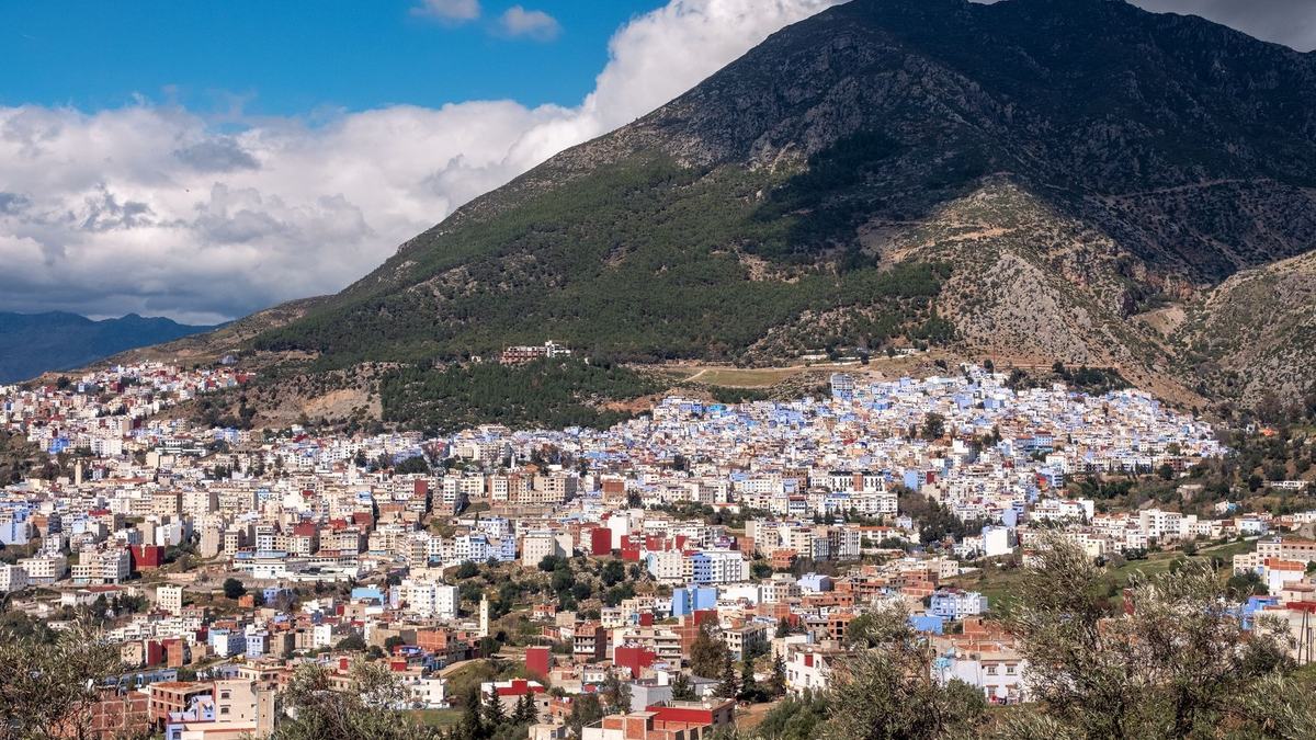The blue town of Chefchaouen below a green mountain under a blue sky