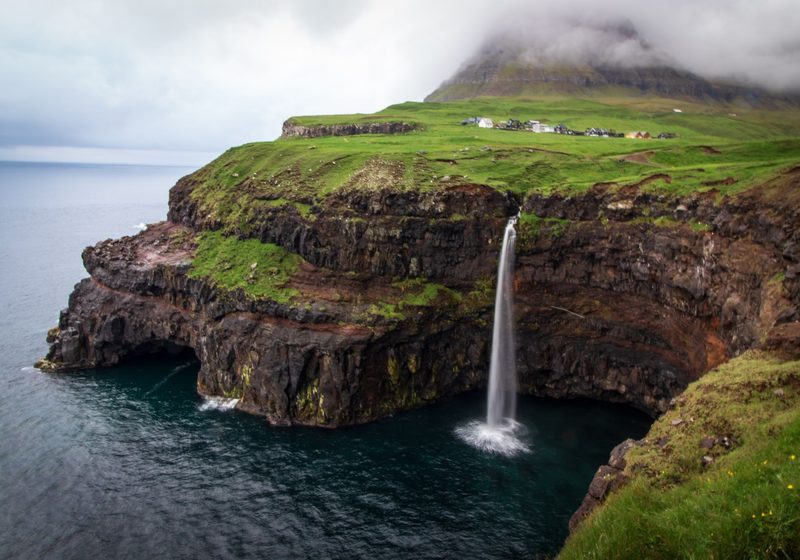A waterfall dropping from a green cliff into the sea