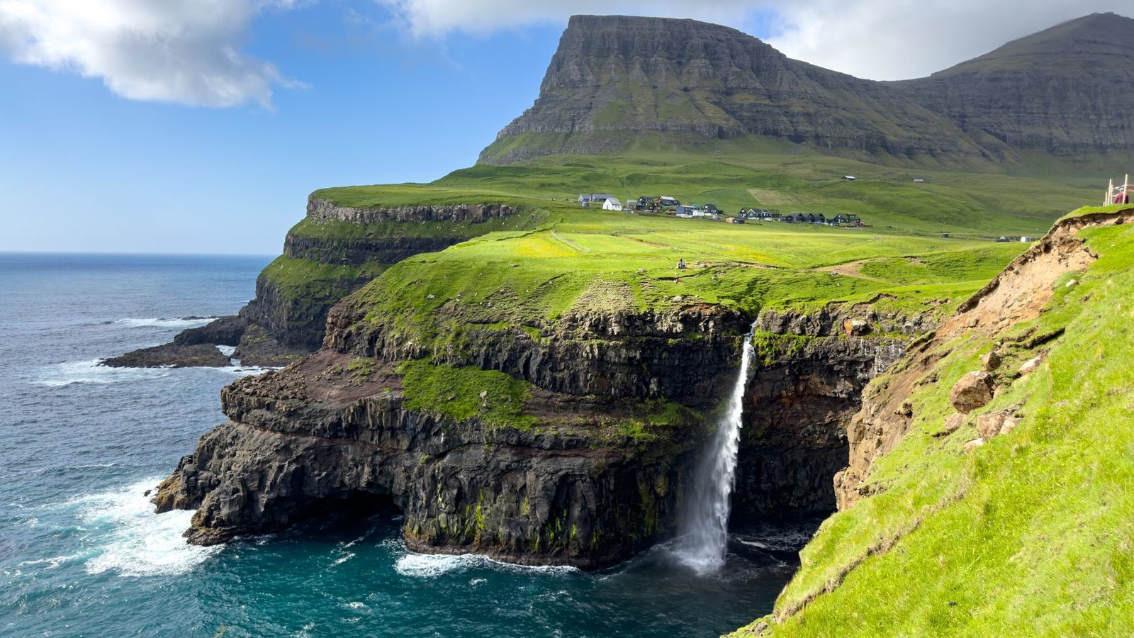 The Múlafossur waterfall falling from a green cliff into the Atlantic beside Gásadalur village