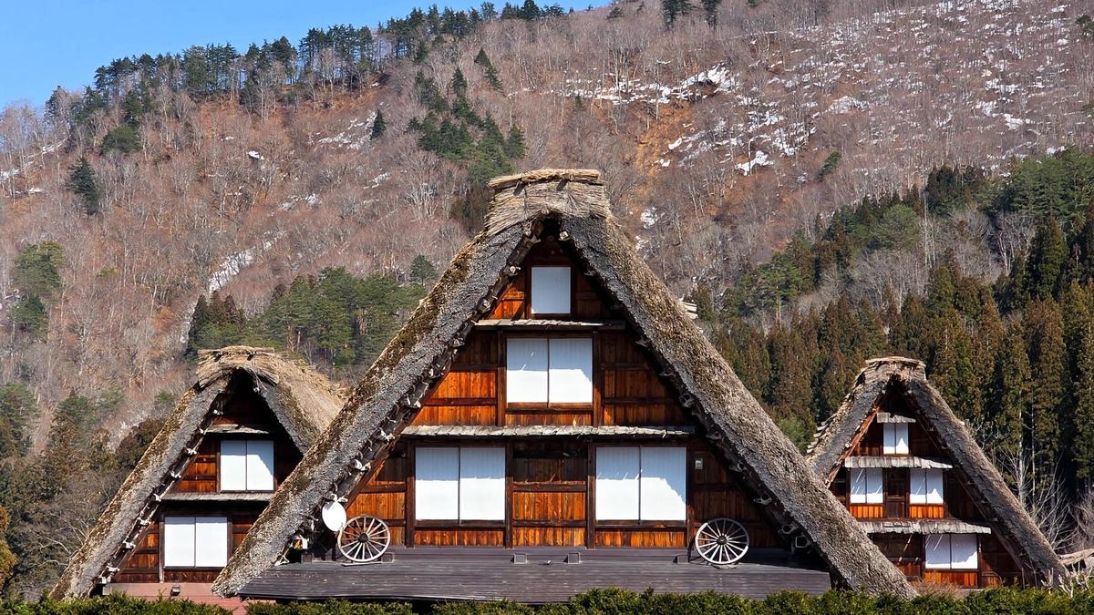 Three thatched gassho-zukuri farmhouses below a mountain