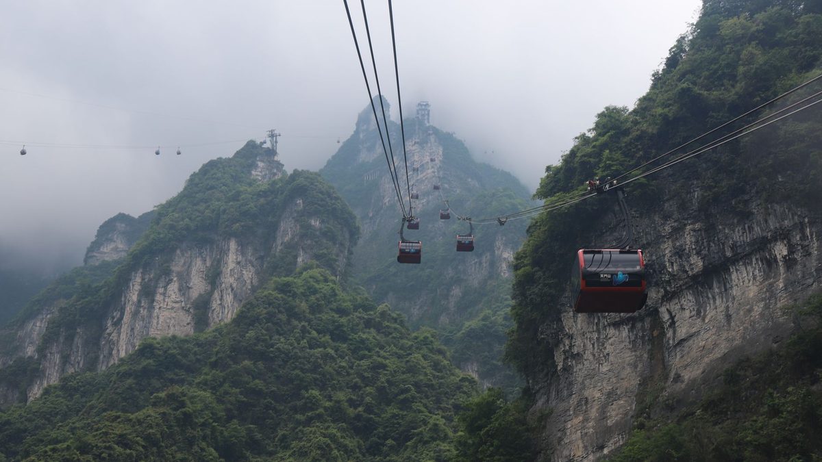 Cable cars climbing over green mountains in mist